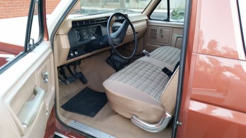 1981 Ford Bronco - Interior view of the driver's side of a vintage Ford Bronco, showing the tan plaid seat, dashboard, steering wheel, and door panel.