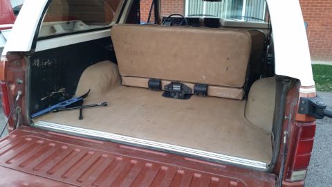1981 Ford Bronco - The rear interior of a vintage Ford Bronco is shown with the tailgate open. A jack and tire iron are visible on the floor of the cargo area.