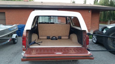 1981 Ford Bronco - The rear of a brown and white Ford Bronco is shown with the tailgate open, revealing the cargo area. A boat on a trailer is visible to the…