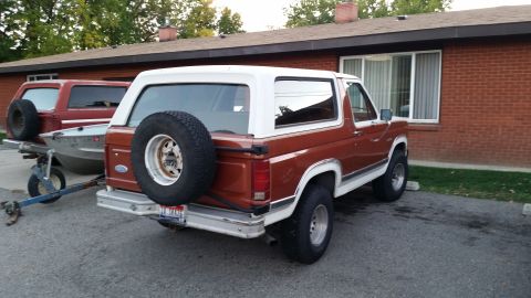 1981 Ford Bronco - The rear passenger side of a brown and white 1981 Ford Bronco is shown parked next to a brick building. A boat on a trailer is hitched to t…