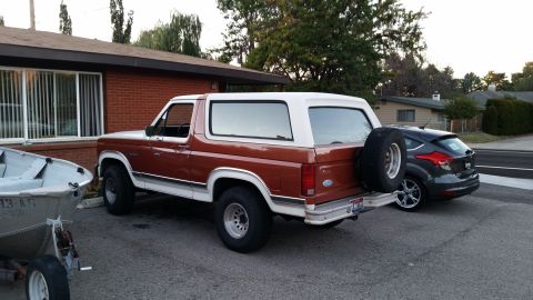 1981 Ford Bronco - A two-tone brown and white Ford Bronco is parked next to a dark gray Ford Focus. A small aluminum boat on a trailer is parked to the left o…