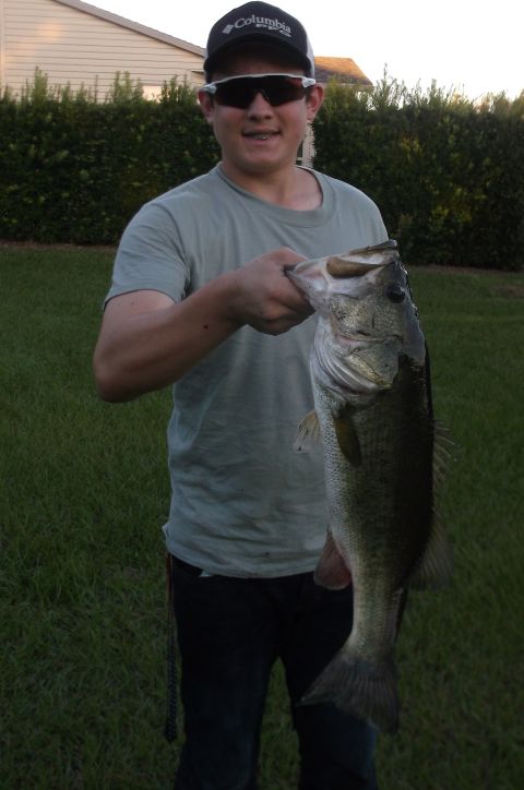 1979 Ford Ranchero - A person is holding a large bass while wearing a Columbia hat and sunglasses. The person is standing in a grassy yard with a hedge and a ho…