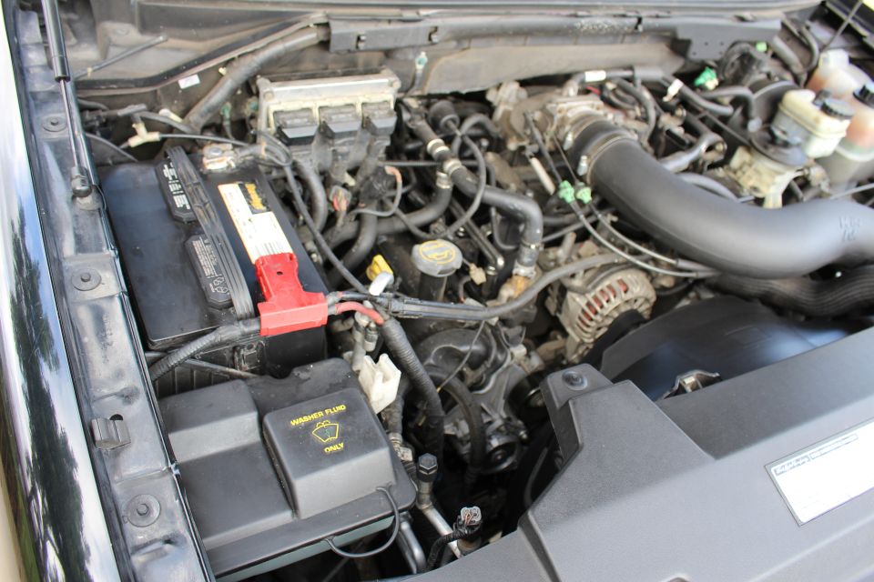 Engine bay of a black Ford Expedition, showing battery, hoses, and washer fluid cap.