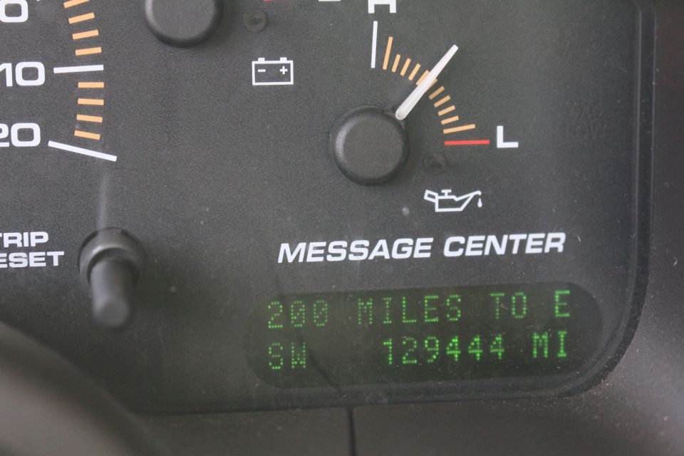 Vehicle dashboard with fuel gauge, battery light, oil light, and digital message center displaying range and odometer.