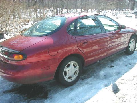 1997 Ford Taurus - A red sedan sits in a snowy area, showing its side profile and rear quarter panel.