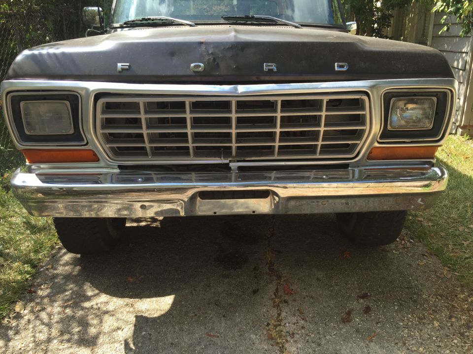 Dark colored Ford truck front grille and bumper, with orange turn signals. Tires visible