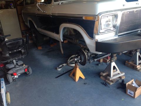 1978 Ford Bronco - A 1978 Ford Bronco is shown on jack stands in a garage, with the front wheel assembly disassembled for maintenance.