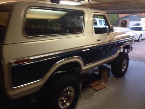 1978 Ford Bronco - A two-tone white and blue Ford Bronco is parked inside a garage with another vehicle visible behind it.