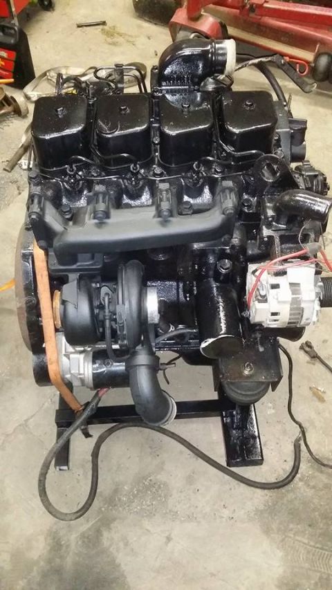 1994 Ford Bronco - A black engine, likely a diesel, is displayed on a stand with its turbocharger and alternator visible.