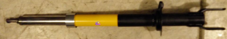 Shock absorber with yellow and black body, mounted on a textured surface