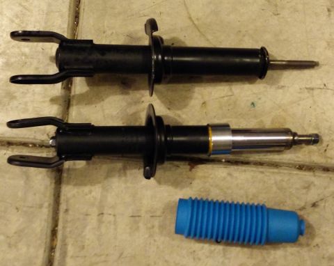 1993 Ford Thunderbird - Two automotive shock absorbers and a blue dust boot are laid out on a concrete floor.