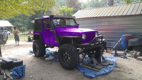 1994 Ford Bronco - A modified purple Jeep Wrangler is elevated on jack stands in an outdoor repair area.