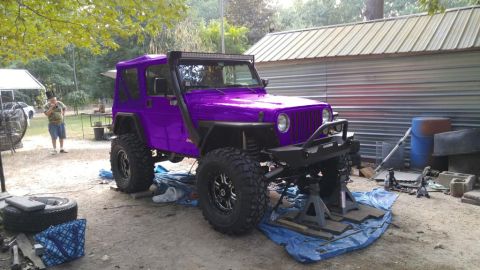 1994 Ford Bronco - Modified purple Jeep Wrangler is elevated on jack stands, an aftermarket bumper and a light bar on the roof.