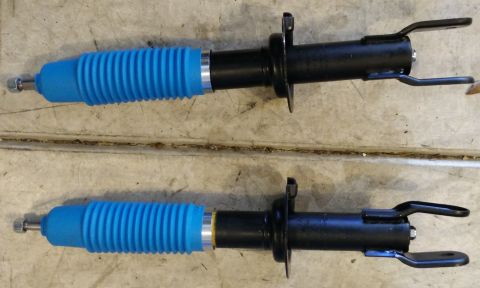 1993 Ford Thunderbird - Pair of shock absorbers with blue bellows and mounting hardware shown on a workbench.