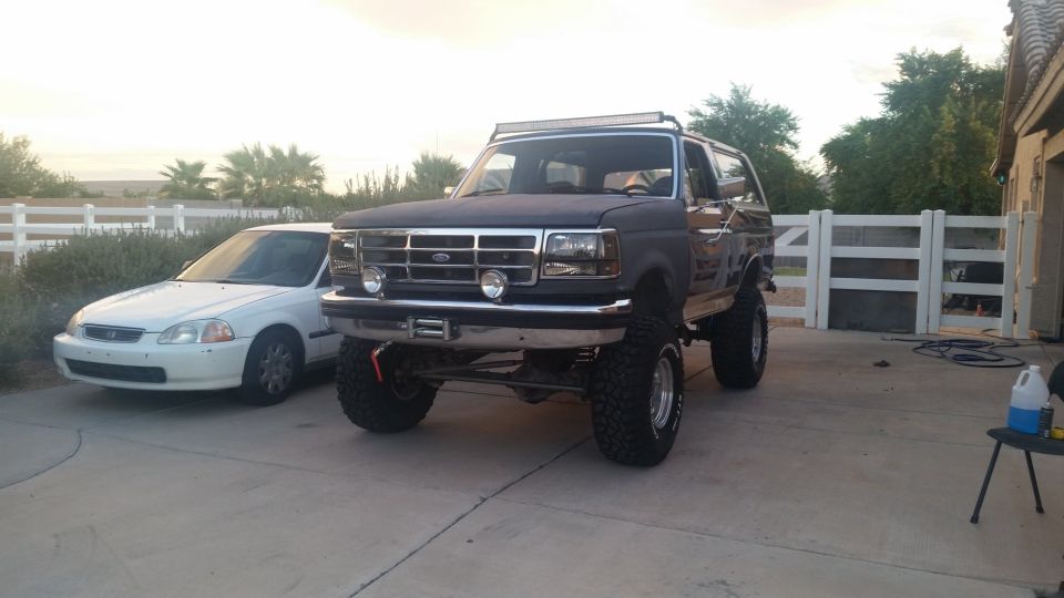 Lifted dark SUV with light bar and winch, parked next to a white sedan