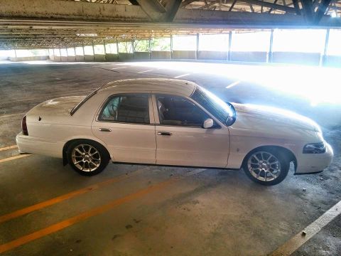2000 Mercury Grand Marquis - Side view of a white 2000 Mercury Grand Marquis parked in a multi-level garage.