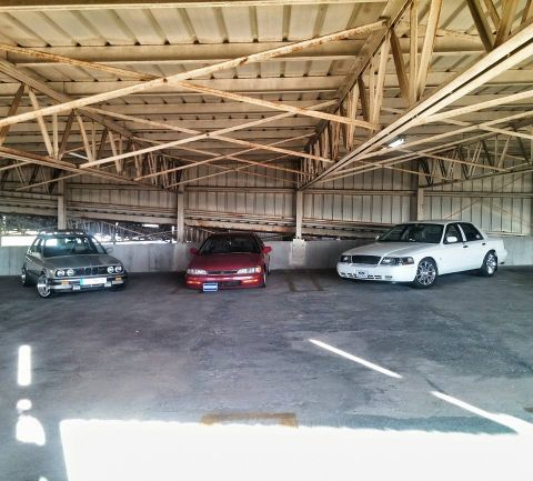 2000 Mercury Grand Marquis - Three cars are parked in an open-air garage with a visible metal roof structure.