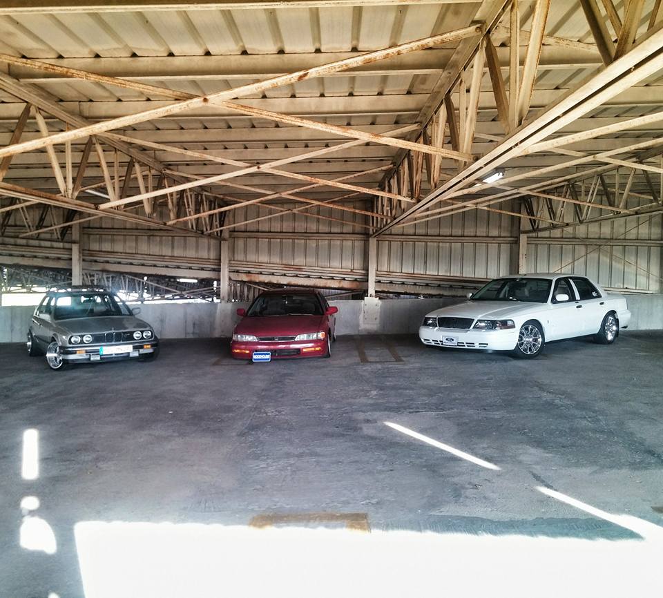 White sedan parked under a metal structure, front view. Chrome grille and wheels are visible