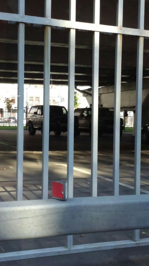 1987 Ford Bronco - A dark 1987 Ford Bronco with a camper shell is parked behind metal bars, with another vehicle visible behind it.