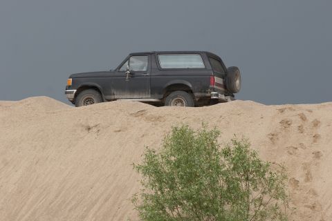 1987 Ford Bronco - A black 1987 Ford Bronco is seen on a sand dune under a cloudy sky.