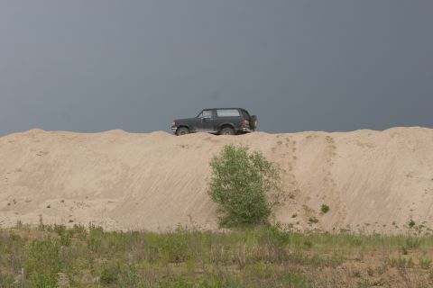 1987 Ford Bronco - A 1987 Ford Bronco is seen cresting a large sand dune under a dark, overcast sky.
