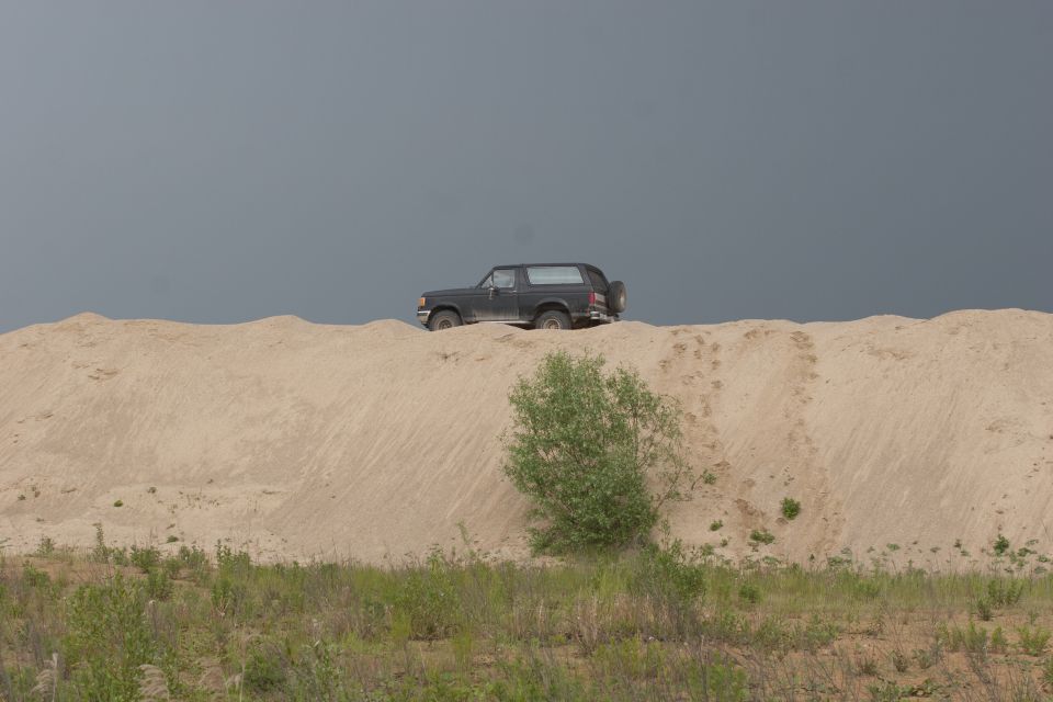 Dark 1987 Ford Bronco on a sand dune under a cloudy sky