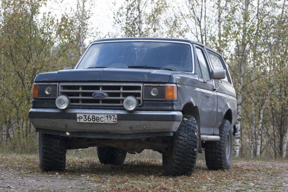 1987 Ford Bronco parked on a dirt road with trees in the background