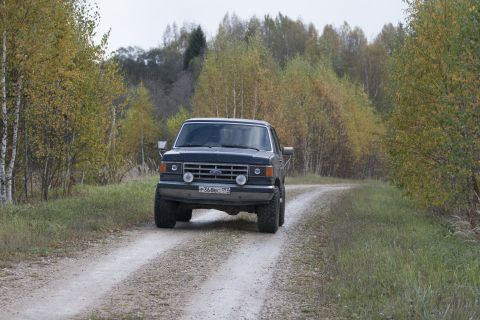 1987 Ford Bronco - 1987 Ford Bronco driving on a dirt road during autumn.