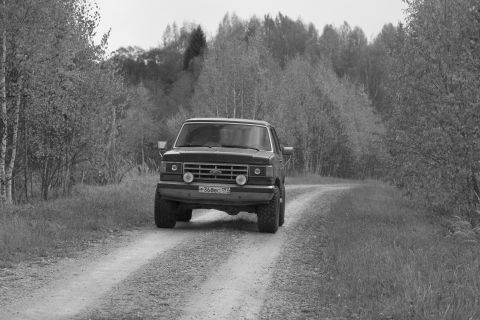 1987 Ford Bronco - A Ford F-Series truck drives down a gravel road surrounded by trees.