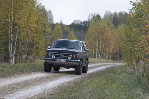 1987 Ford Bronco - A dark blue 1987 Ford Bronco navigates a dirt road surrounded by trees in autumn.