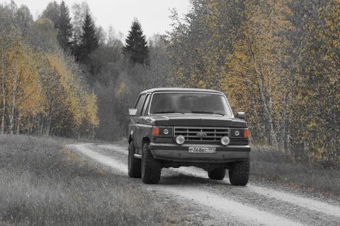 1987 Ford Bronco - 1987 Ford Bronco navigates a gravel road surrounded by fall foliage.