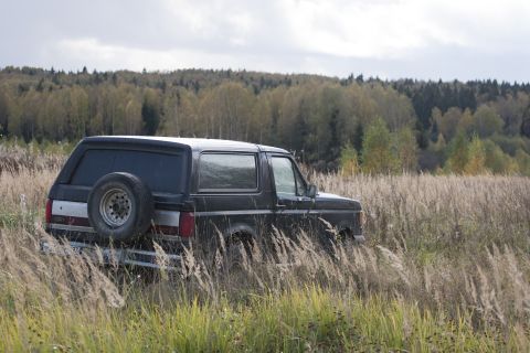 1987 Ford Bronco - A 1987 Ford Bronco sits in a field of dry grass, with a forest in the background.