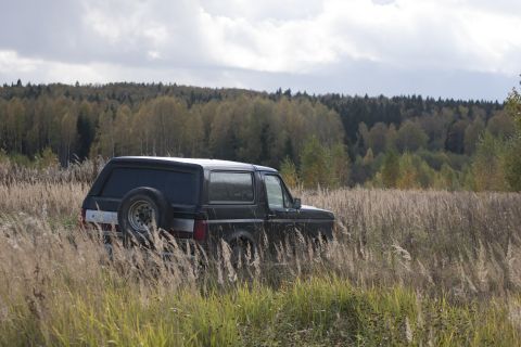 1987 Ford Bronco - A black 1987 Ford Bronco is parked in a field of tall grass with a forest in the background under a cloudy sky.