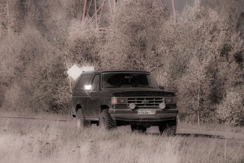 1987 Ford Bronco - A black 1987 Ford Bronco is parked on a grassy area with trees in the background.