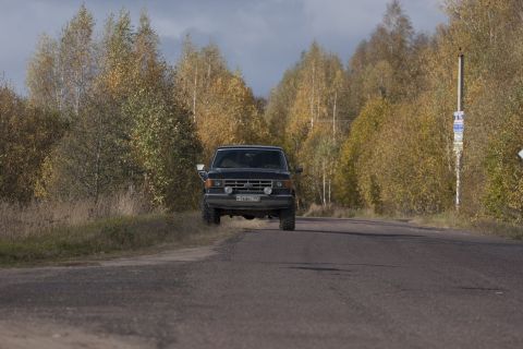 1987 Ford Bronco - A black 1987 Ford Bronco is seen driving on a road surrounded by trees in autumn.