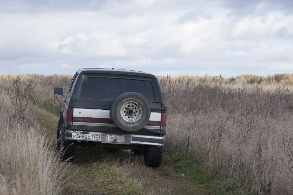 1987 Ford Bronco rear view, driving on a dirt path in a field of dry grass