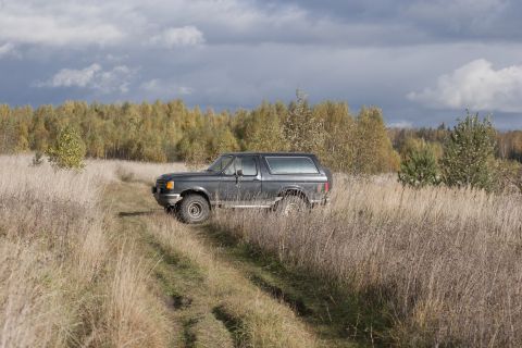 1987 Ford Bronco - A 1987 Ford Bronco drives through a field of dry grass under a cloudy sky.