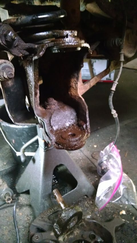 1994 Ford Bronco - This heavily corroded suspension part is being worked on, with a brake line hanging nearby.