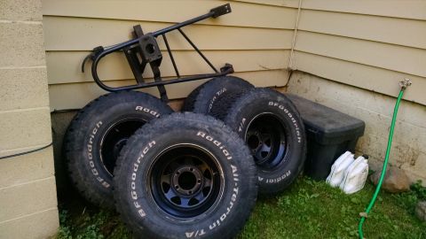 1994 Ford Bronco - Four BFGoodrich All-Terrain T/A tires and a metal rack are stored outside next to a building.