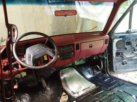 1989 Ford Bronco - The interior of a 1989 Ford Bronco shows a red dashboard and a disassembled door panel, indicating ongoing work or restoration.