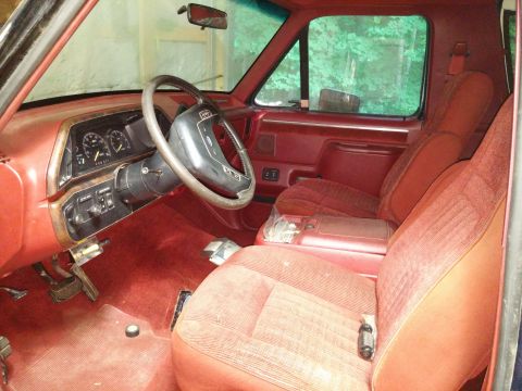 1989 Ford Bronco - The interior of a truck shows red upholstery on the seats and carpeting, with the dashboard and steering wheel in view.