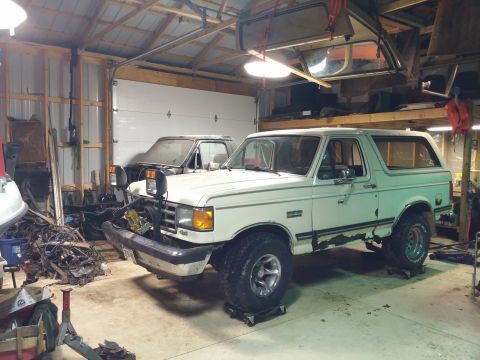 1989 Ford Bronco - A white Ford Bronco is parked in a garage, with another vehicle visible behind it.