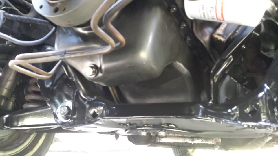 Underside view of a car's engine oil pan and suspension components. A white oil filter is visible