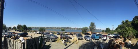 1946 Jeep Willys - A panoramic view of a parking lot filled with various vehicles, overlooking a calm body of water under a clear blue sky.