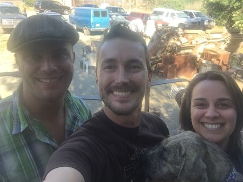 1946 Jeep Willys - A group selfie with multiple vehicles and scrap metal in the background, including a Supermotors logo.