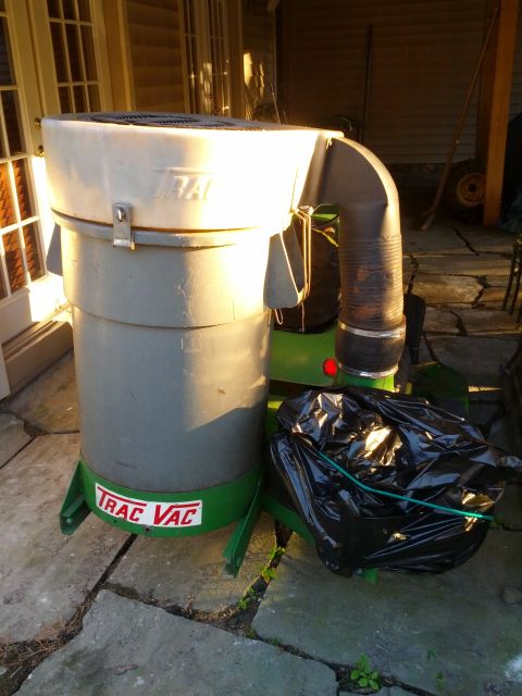 1982 Kubota RTV900 - A Trac Vac leaf vacuum unit is shown outdoors on a stone patio, with a black trash bag tied to its side.