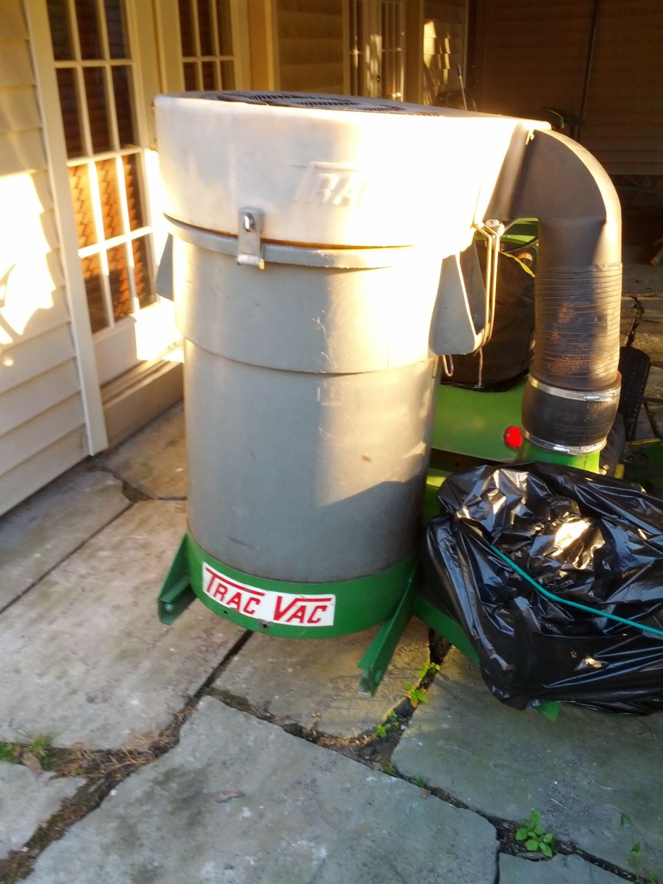 Green and gray Trac Vac leaf vacuum with a black trash bag attached, resting on a stone patio