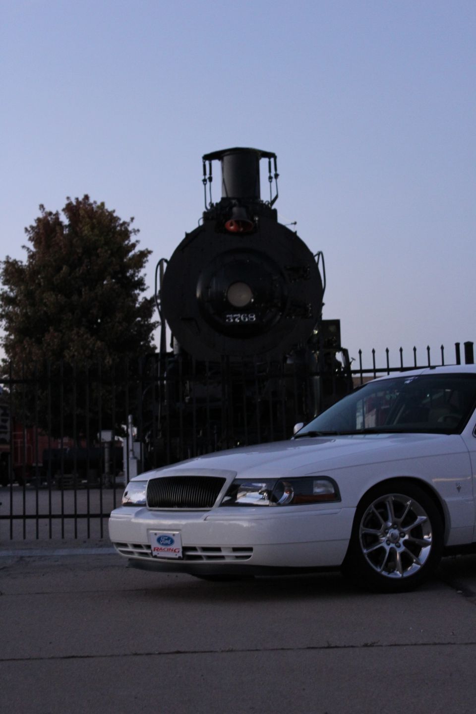 White sedan front view parked before a black steam locomotive