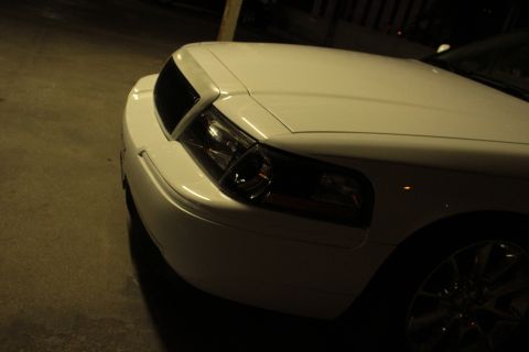 2000 Mercury Grand Marquis - The front end of a white sedan is shown at night, with the headlight and grille in focus.