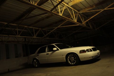2000 Mercury Grand Marquis - A white sedan with aftermarket wheels and grille is parked indoors under a metal roof.